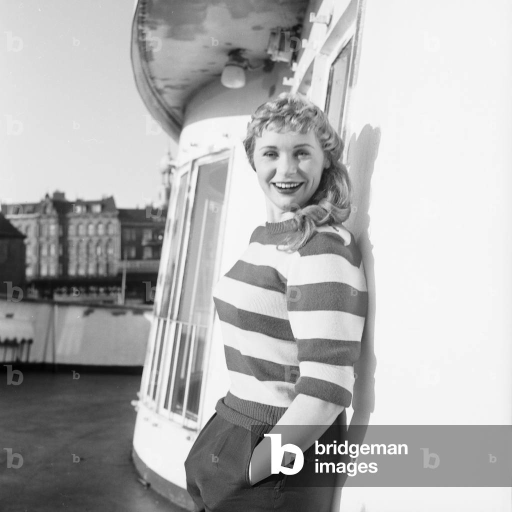 A young female member of the cast of the Hamburg Ohnsorg Theatre leaning at the cabin of the ship 