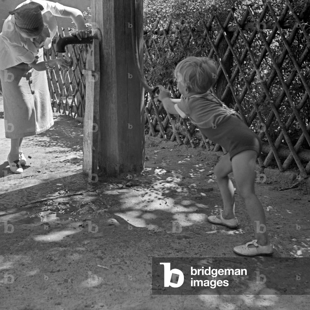 A little boy pumping up water for his mother, Germany 1930s (b/w photo)