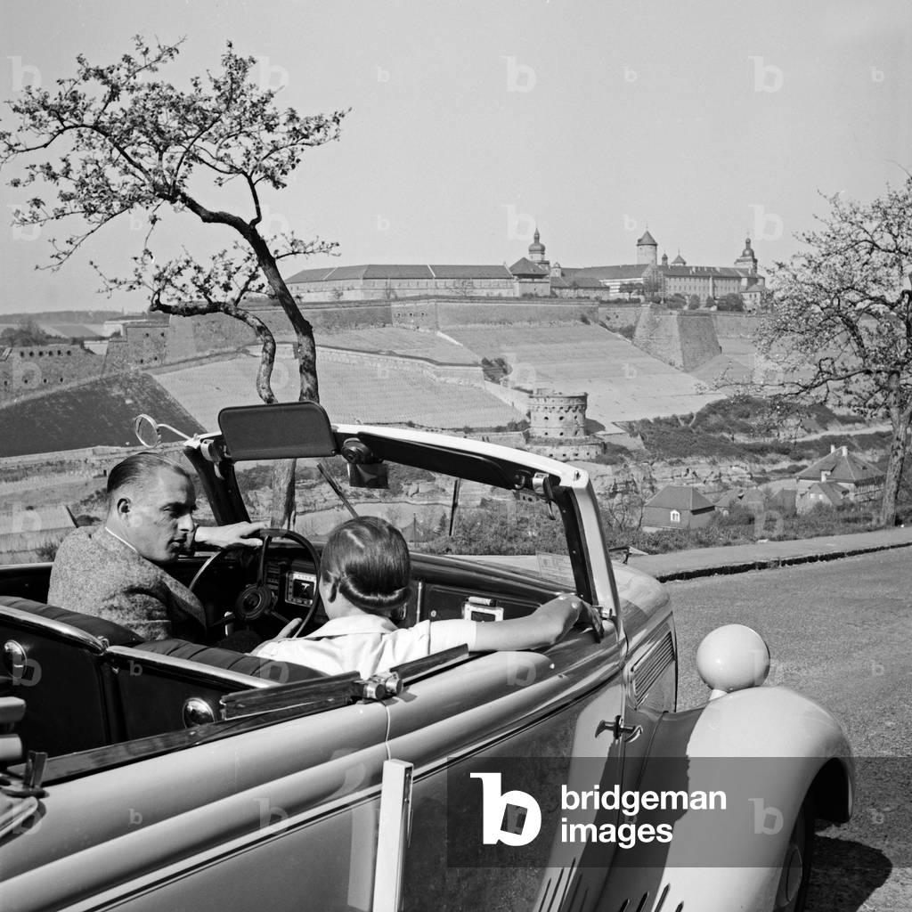 A man and a woman in a convertible heading to Marienberg fortress at Wuerzburg, Germany 1930s (b/w photo)