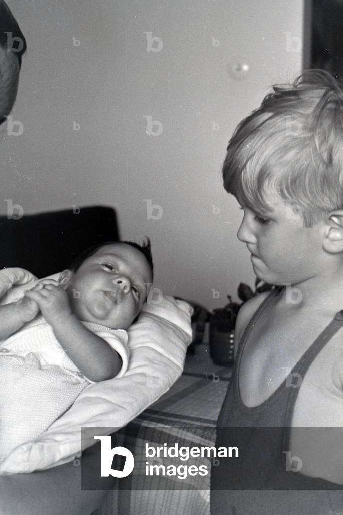 A boy is regarding a baby, which is hold by a woman, Germany 1930s (b/w photo)