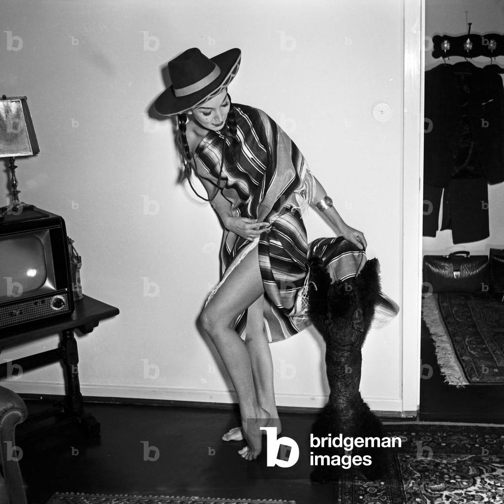 doing a promotional photo shoot wearing a poncho and a sombrero hat with her poodle, Germany 1950s
