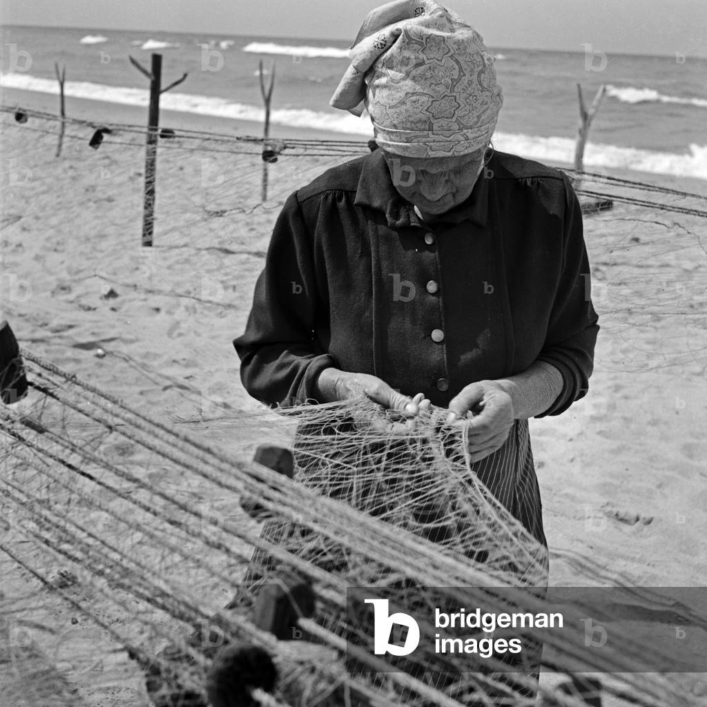 A fisherwoman repairing her nets on the shore at Rositten at the Preussisch Eylau district in East Prussia, Germany 1930s (b/w photo)