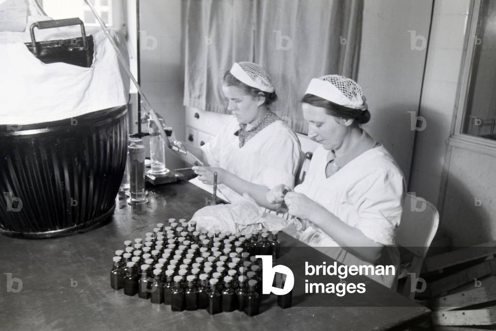 Two lab assistants are filling up medication into little bottles in the laboratory of the Behringwerke, Marburg, Germany 1930s (b/w photo)