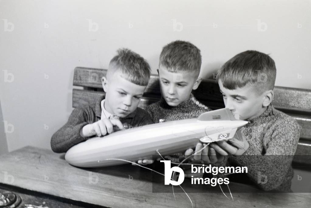 Three school boys are curiously examining a zeppelin model that has a swastika painted on its elevator, zeppelin village near Frankfurt am Main, Germany 1930s (b/w photo)