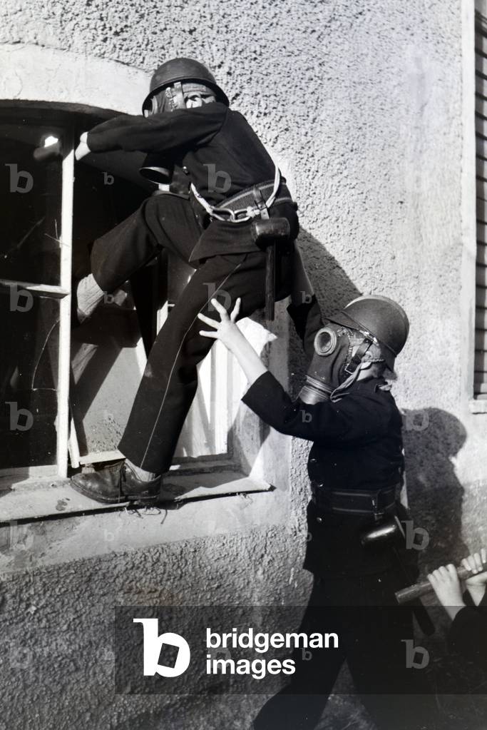 Boys with smoke helmets climbing through a window during a training of the junior firefighters, Germany 1930s (b/w photo)