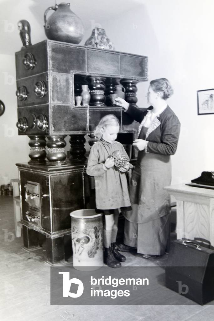 A master potter is showing a finished stoneware jug to a little girl, Germany 1930s (b/w photo)
