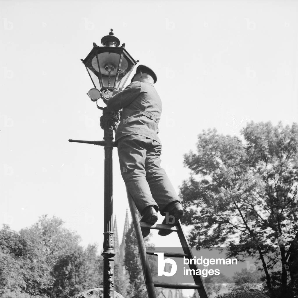 A public servant changing broken bulbs from a street lantern, Germany 1930s (b/w photo)