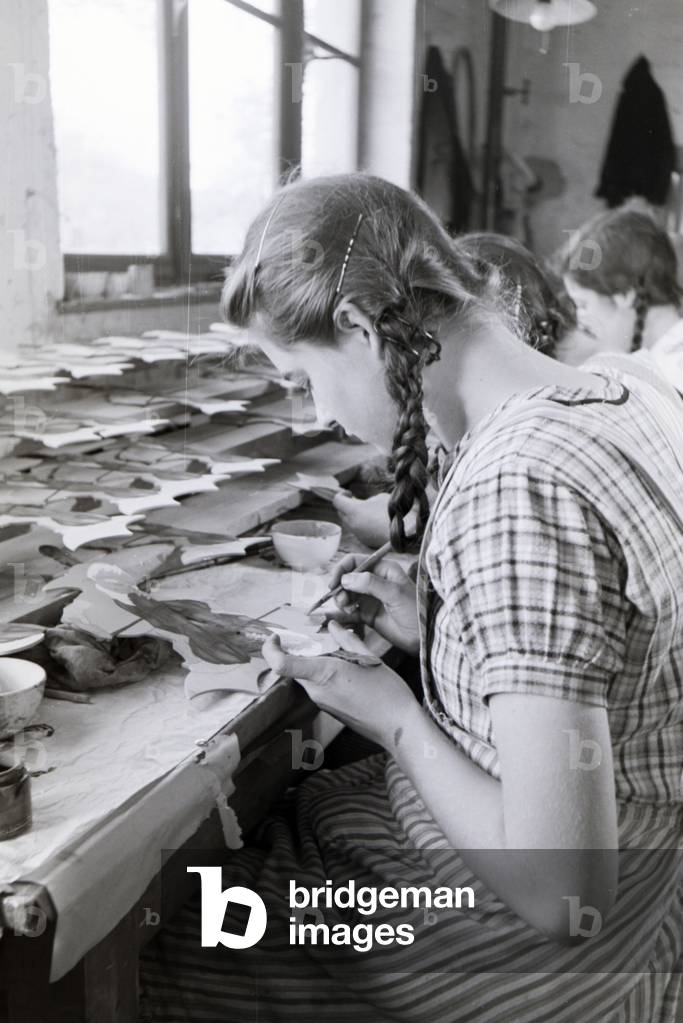 An employee of the Heller Kunst workshops in the Eifel painting a sawn out wooden figure, Germany 1930s (b/w photo)