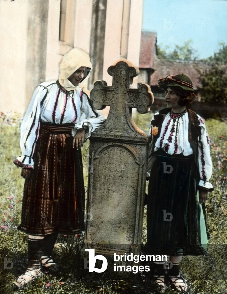 Two girls standing by a tombstone on a churchyard in Romania