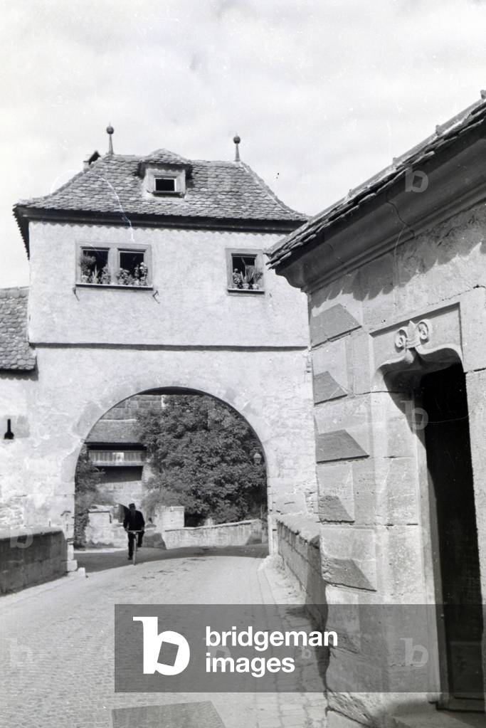 A cyclist driving through one of the many historical archways in Rothenburg ob der Tauber, Germany 1930s (b/w photo)