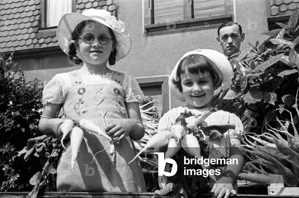 Parade float of the radish dispatch company Hanacker with a staff member and two little girls at the pageant of the annual radish fair at Schifferstadt, Germany 1930s (b/w photo)