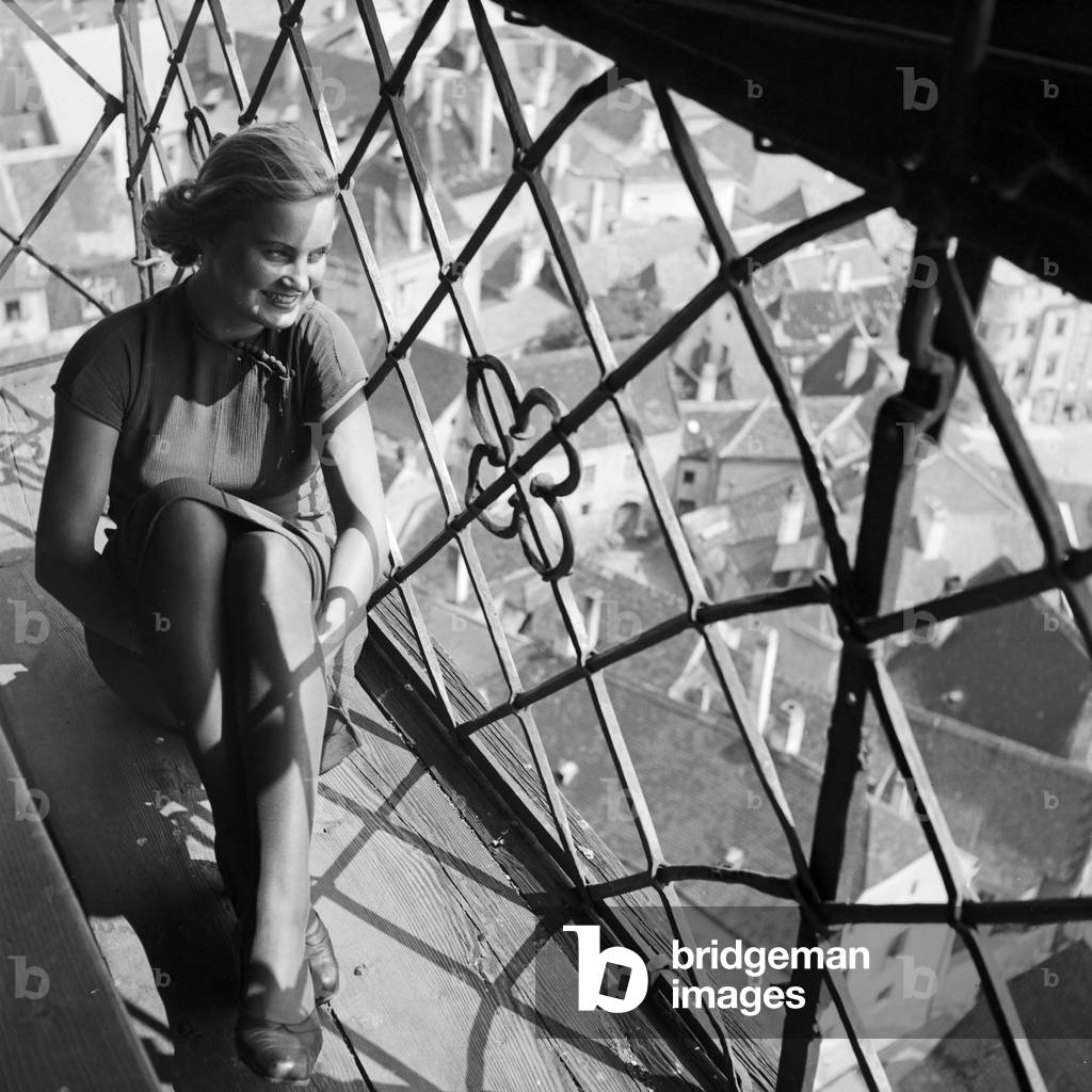 A young woman sitting on the window ledge of a beldry watching down on the city, Germany 1930s (b/w photo)