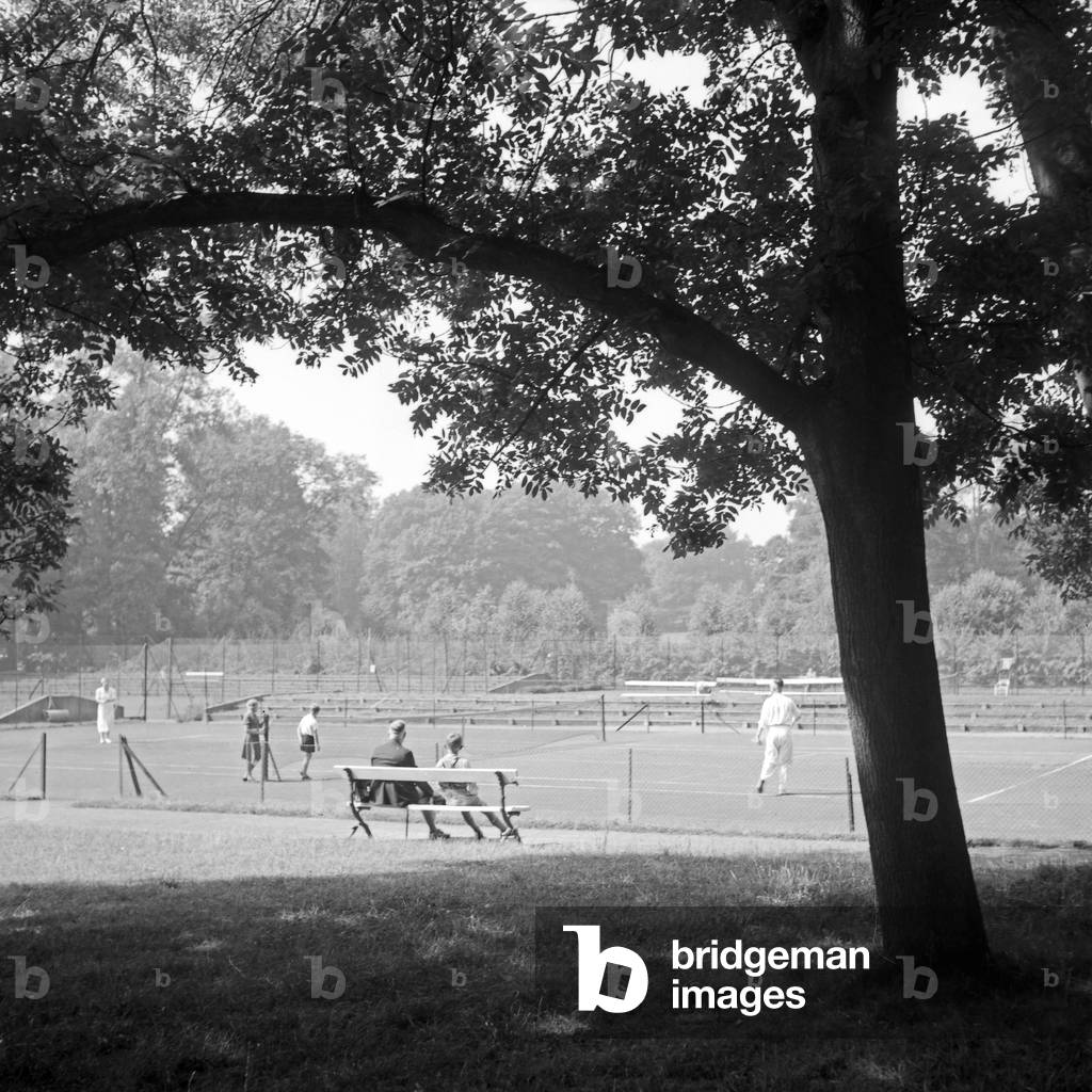 A couple watching a tennis match from a bench at Bad Homburg, Germany 1930s (b/w photo)