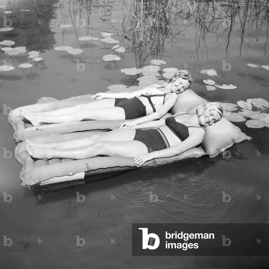 Two young women on an air matress on a lake in the Wachau area in Austria, Germany 1930s (b/w photo)