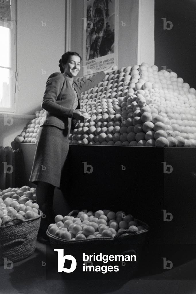 Employee of the Leipziger Frühjahrsmesse in front of a stand with spanish oranges, Germany 1941 (b/w photo)