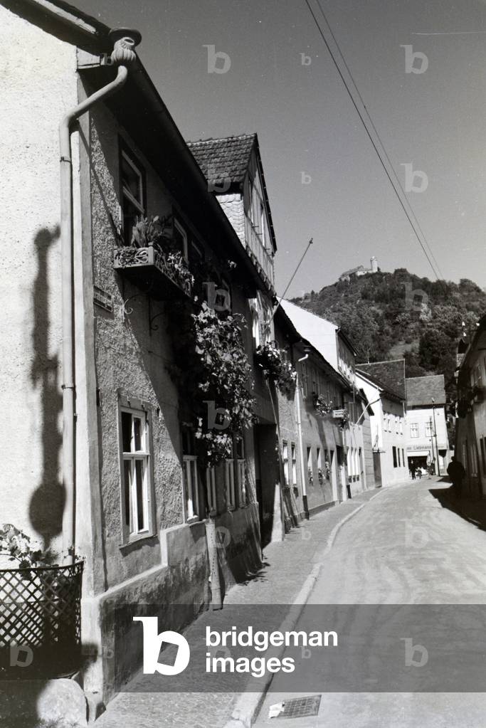 A street with apartment buildings with the Grafenstein castle in the background, Bad Blankenburg, Germany 1930s (b/w photo)