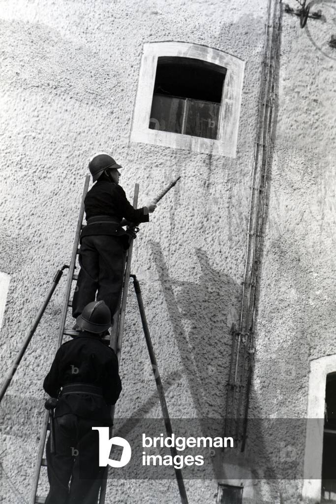 Two boys of the junior firefighters standing on a ladder with the water hose during a firefighter training, Germany 1930s (b/w photo)