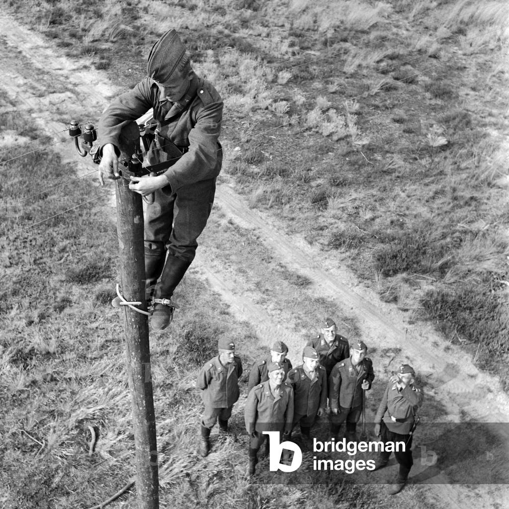 A soldier of the pioneer construction group nealry on top of a telegraph mast, Germany 1940s (b/w photo)