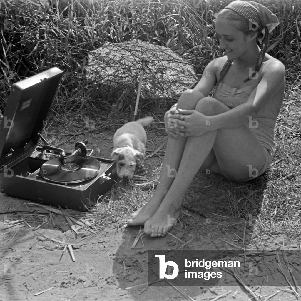 Advertising: a young woman and a puppy sitting at the beach listening to a gramophone, Germany 1930s (b/w photo)
