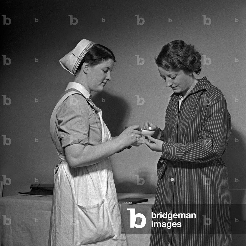 A young nurse of the German Red Cross applying a pill to an ill woman, Germany 1930s (b/w photo)