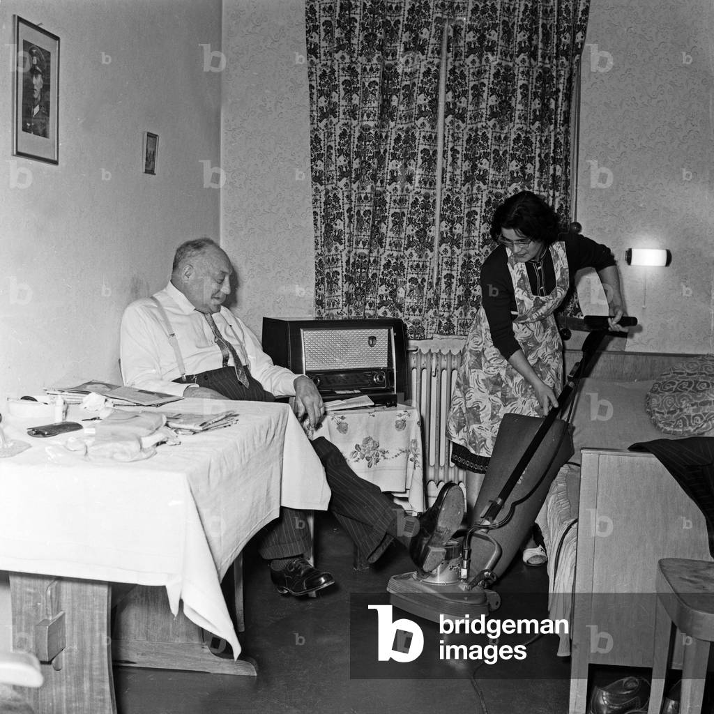A cleaning woman with her vacuum cleaner at he room of an inhabitant of the Stiftung Seefahrtsdank old sailor's home at Hamburg, Germany 1960s