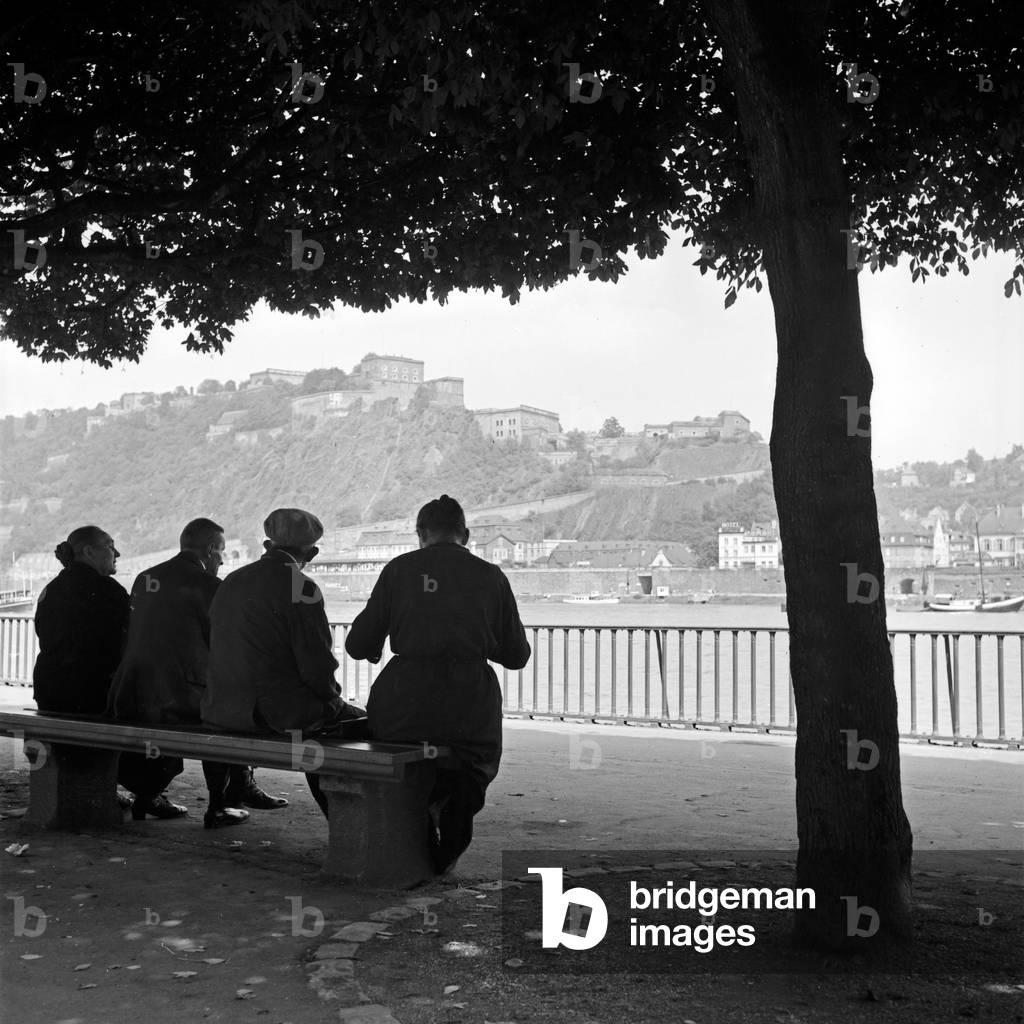 People sitting on the shore of river Rhine and watching Ehrenbreitstein fortress at Koblenz, Germany 1930s (b/w photo)
