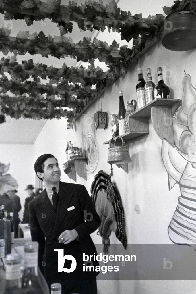 A barkeeper behind a counter with traditional drinks on the Leipziger Frühjahrsmesse, Germany 1941 (b/w photo)