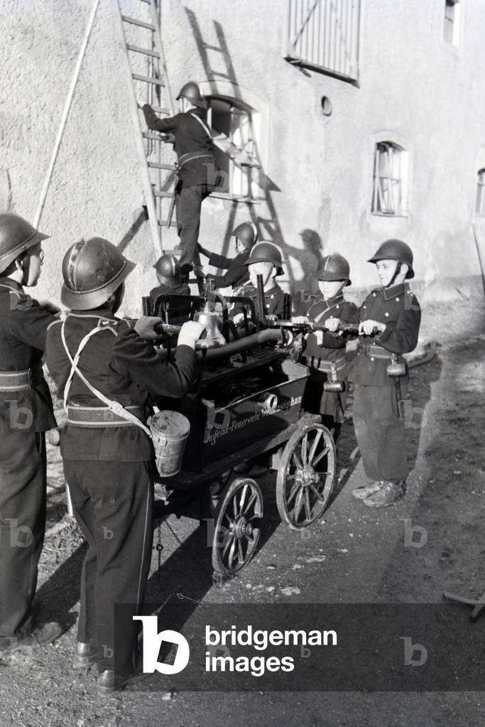 A group of junior firefighters is preparing the firewagon and ladder during a firefighter training, Germany 1930s (b/w photo)