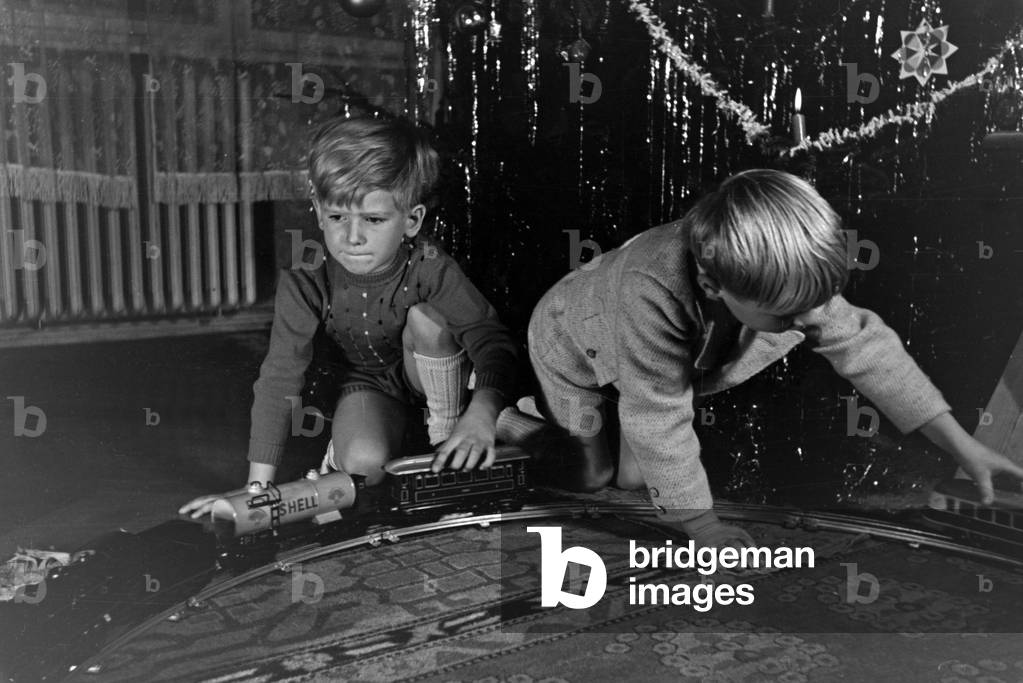 Two boys playing with the new model train under the christmas tree, Germany 1930s (b/w photo)