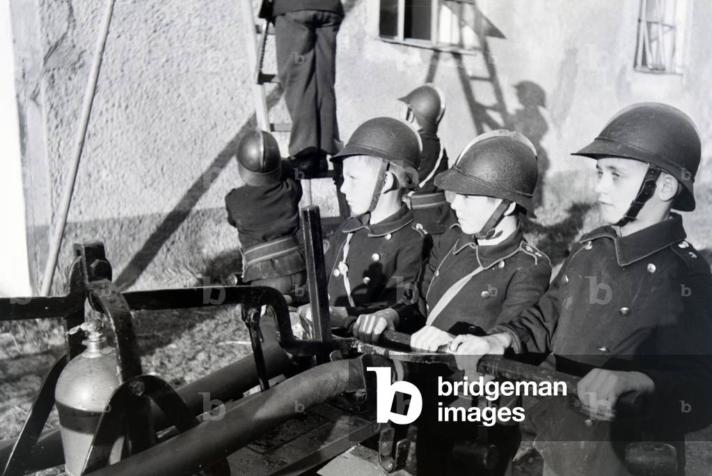 A group of junior firefighters is preparing a ladder during a firefighter training, Germany 1930s (b/w photo)