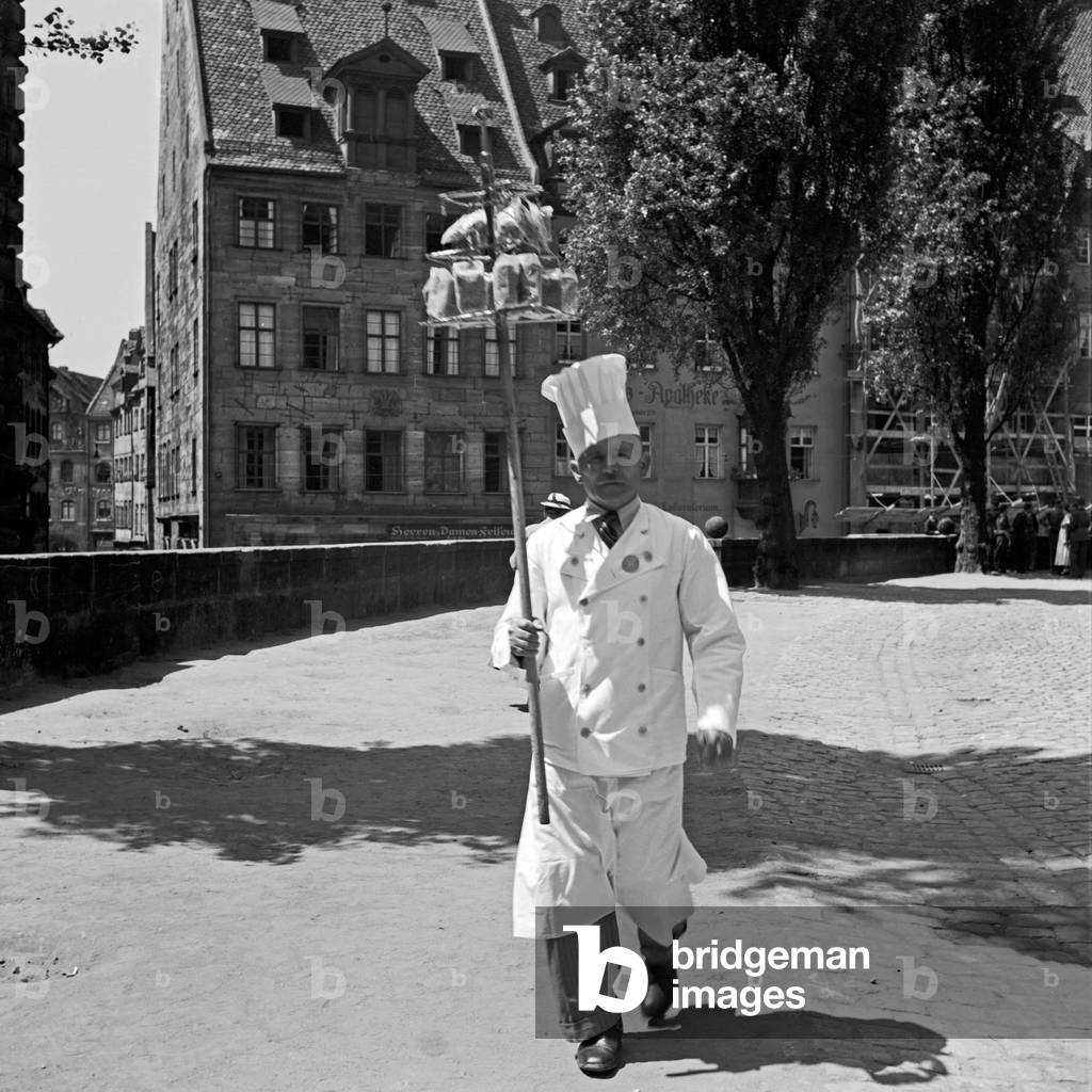 A cook walking through the old city of Nuremberg, Germany 1930s (b/w photo)