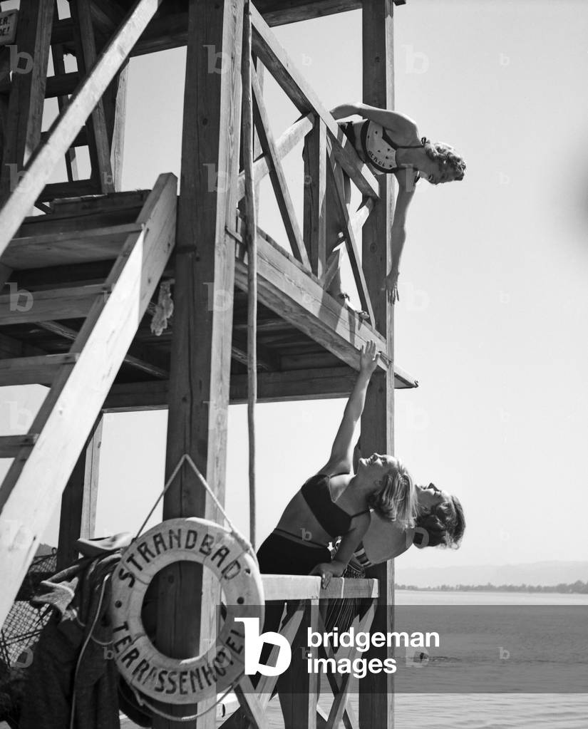 Three young woman on a diving platform on the shore of a lake in the Wachau area in Austria, Germany 1930s (b/w photo)
