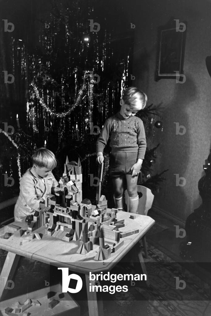 Two boys playing with the new set of toy blocks under the christmas tree, Germany 1930s (b/w photo)