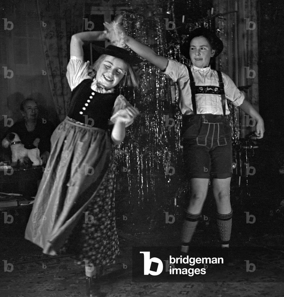 Two girls dressed in Bavarian array and dancing in front of the christmas tree, Germany 1930s (b/w photo)