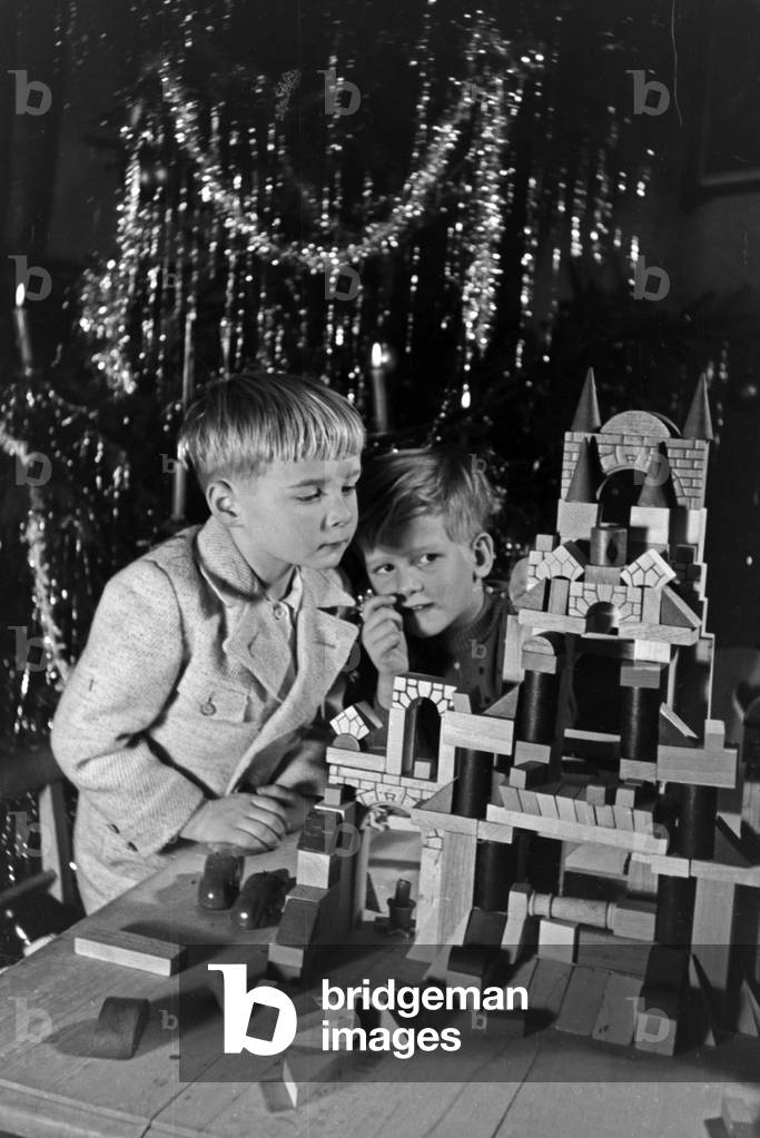 Two boys playing with the new set of toy blocks under the christmas tree, Germany 1930s (b/w photo)
