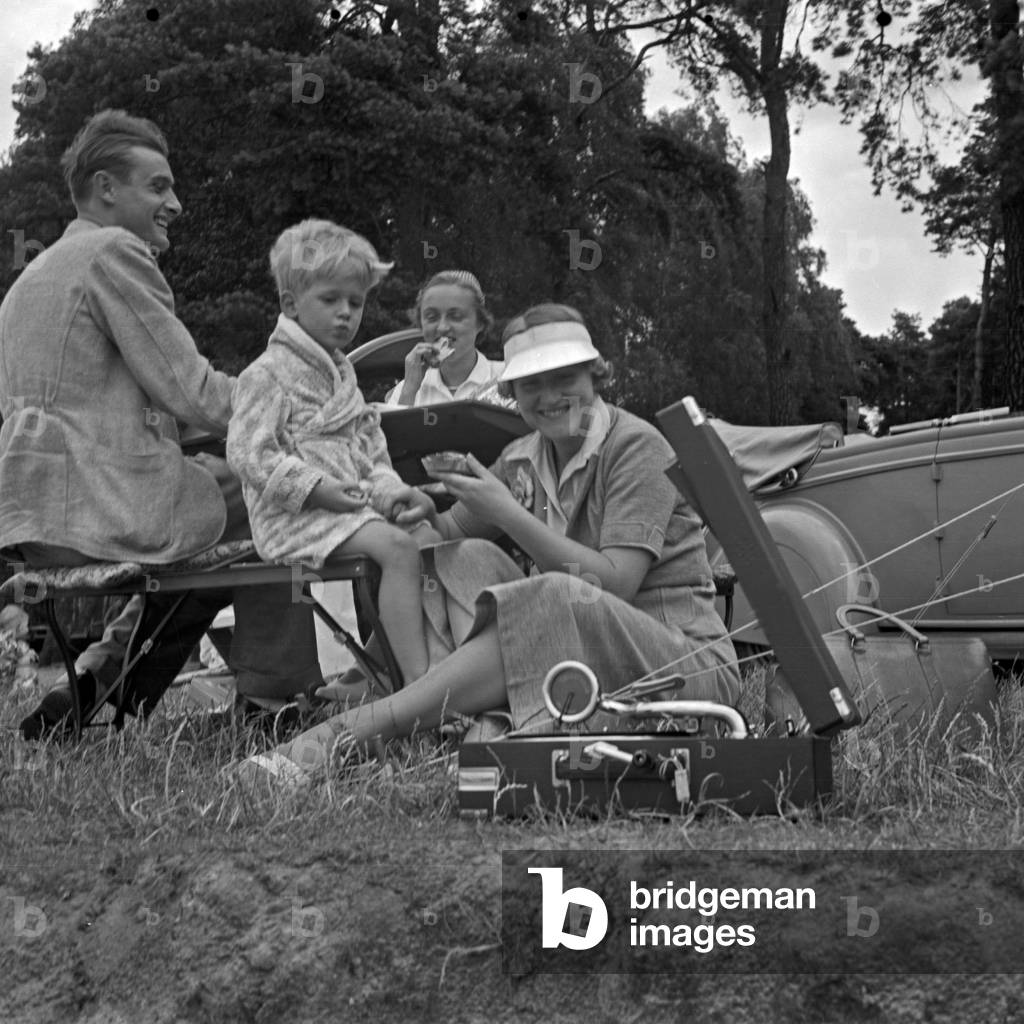 A man, a little boy and two women sitting at a folding table in front of a tent, Germany 1930s (b/w photo)