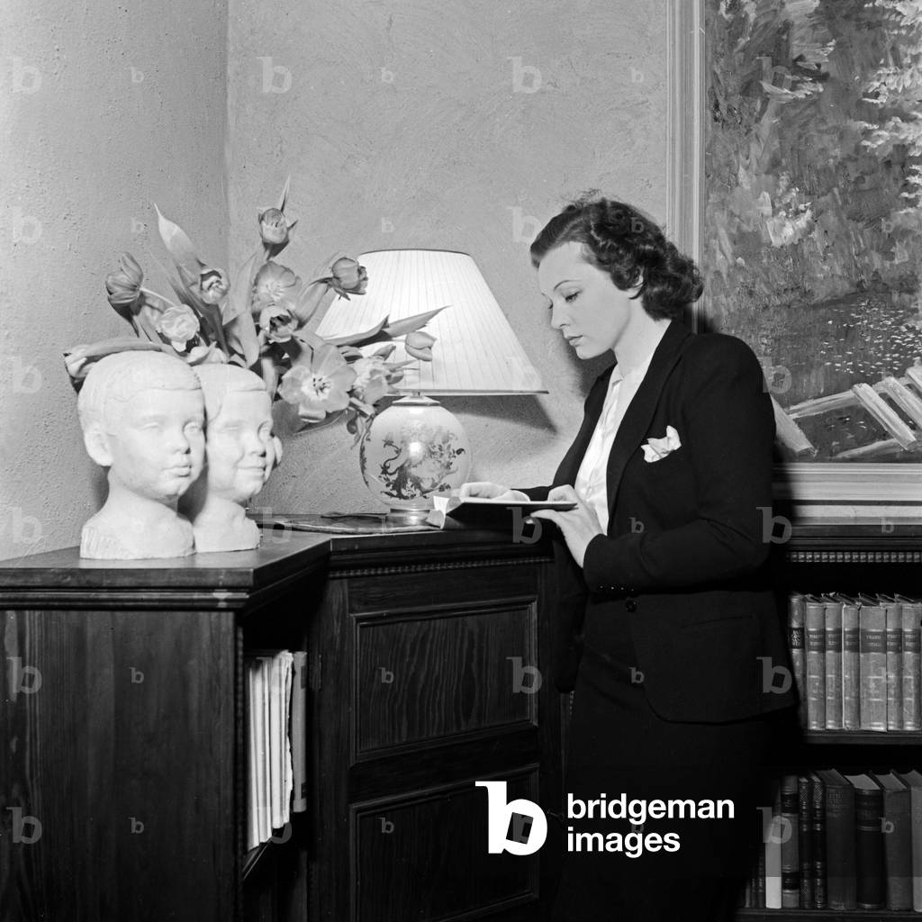 Swedish singer and actress Zarah Leander at a bookshelf with the busts of her two children in her house at Berlin, Germany 1930s (b/w photo)