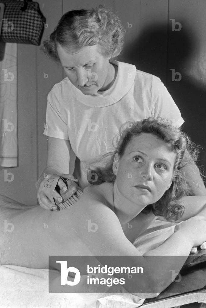 A young woman gets a massage with a brush at Admiralsbad bath in Berlin, Germany 1930s (b/w photo)