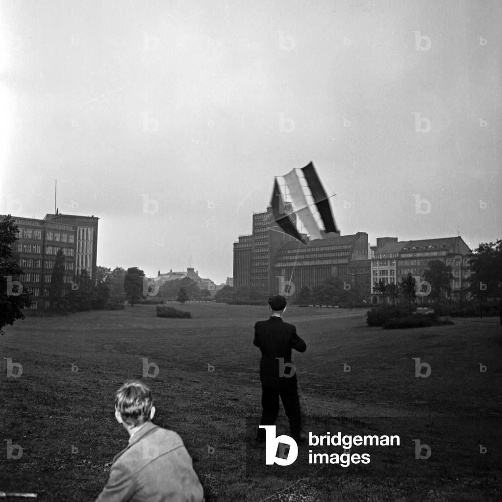 An elder man flying a kite with some children, Germany 1950s