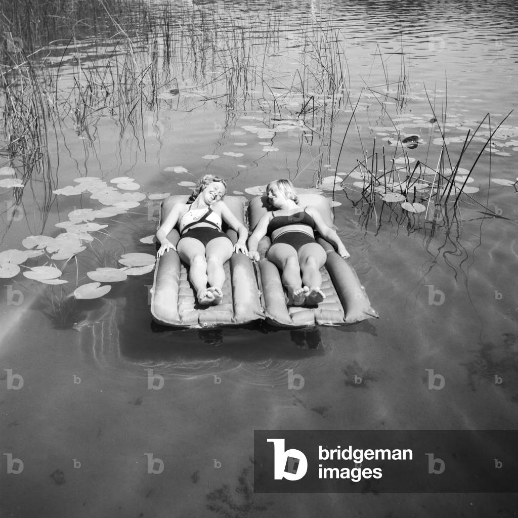 Two young women on an air matress on a lake in the Wachau area in Austria, Germany 1930s (b/w photo)