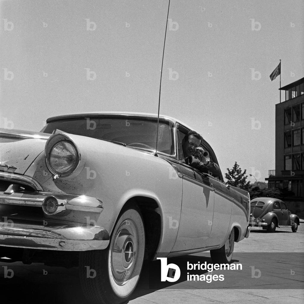 Swiss musician, singer and bandleader Hazy Osterwald driving and playing his trumpet, Germany 1950s