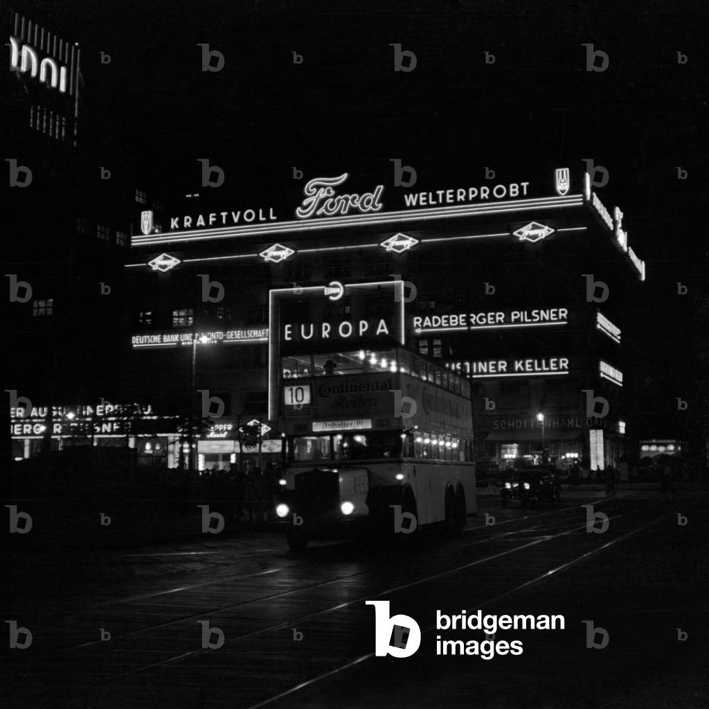 A Berlin bus in front of the illumninated Europapalast building by night, Germany 1930s (b/w photo)