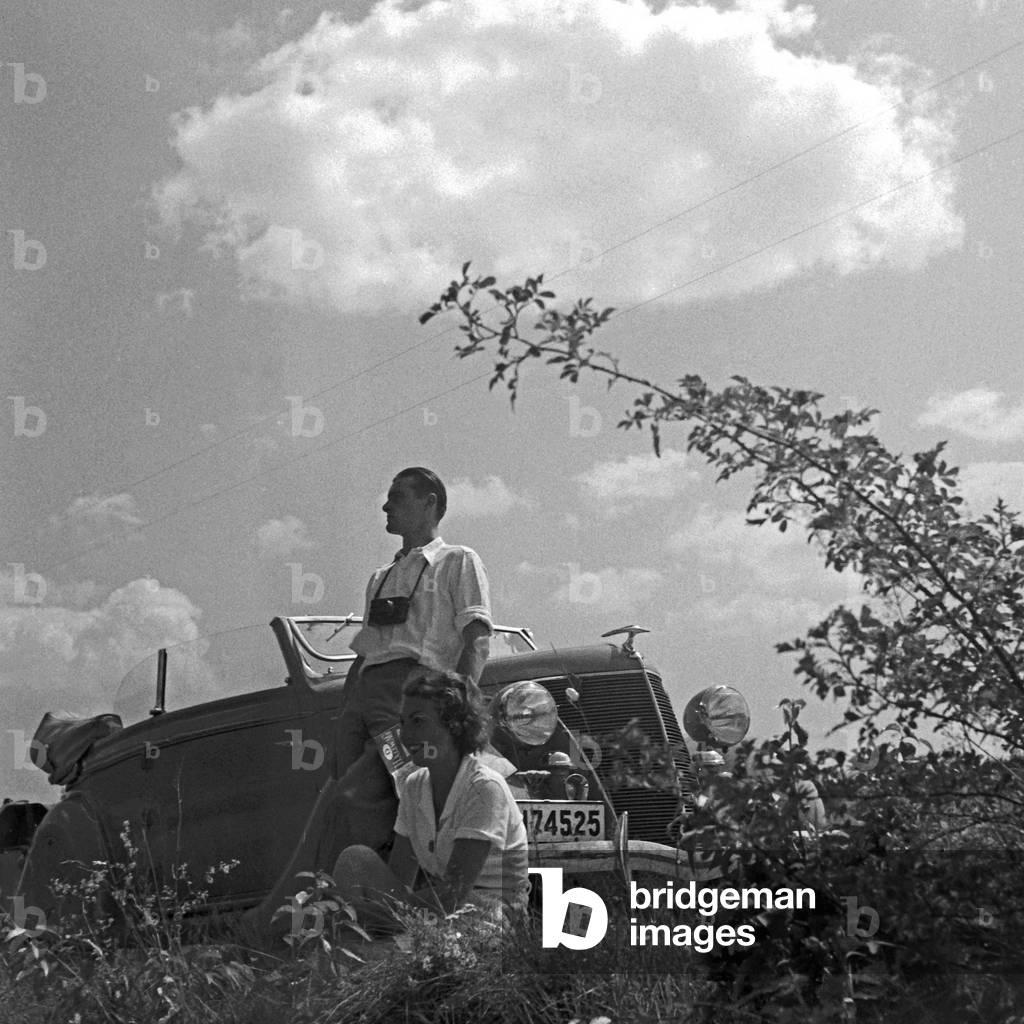A man and a woman resting in front of their convertible, Germany 1930s (b/w photo)
