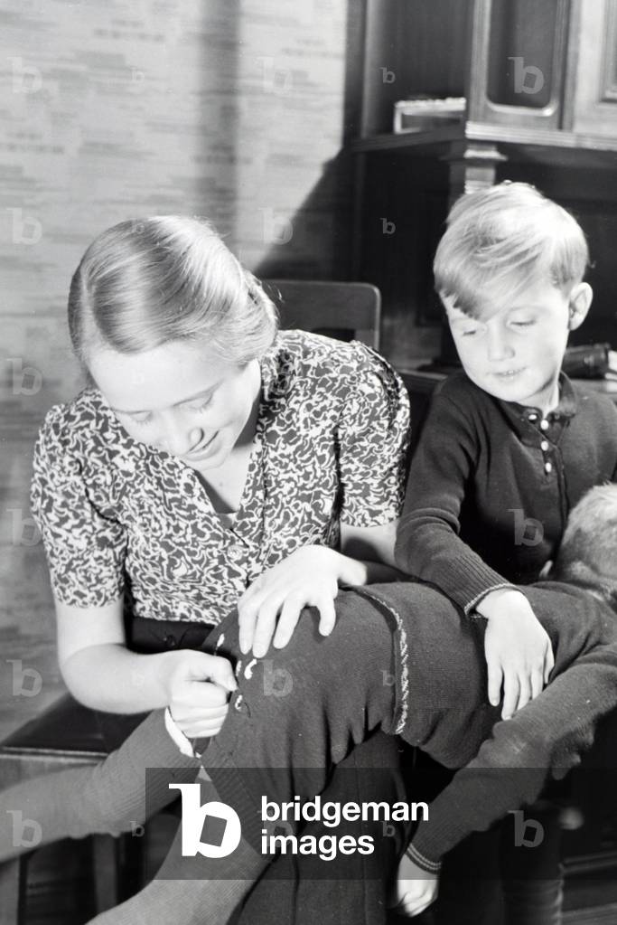 The eldest daughter of a extended family repairing the trousers of her little brother, Germany 1930s (b/w photo)