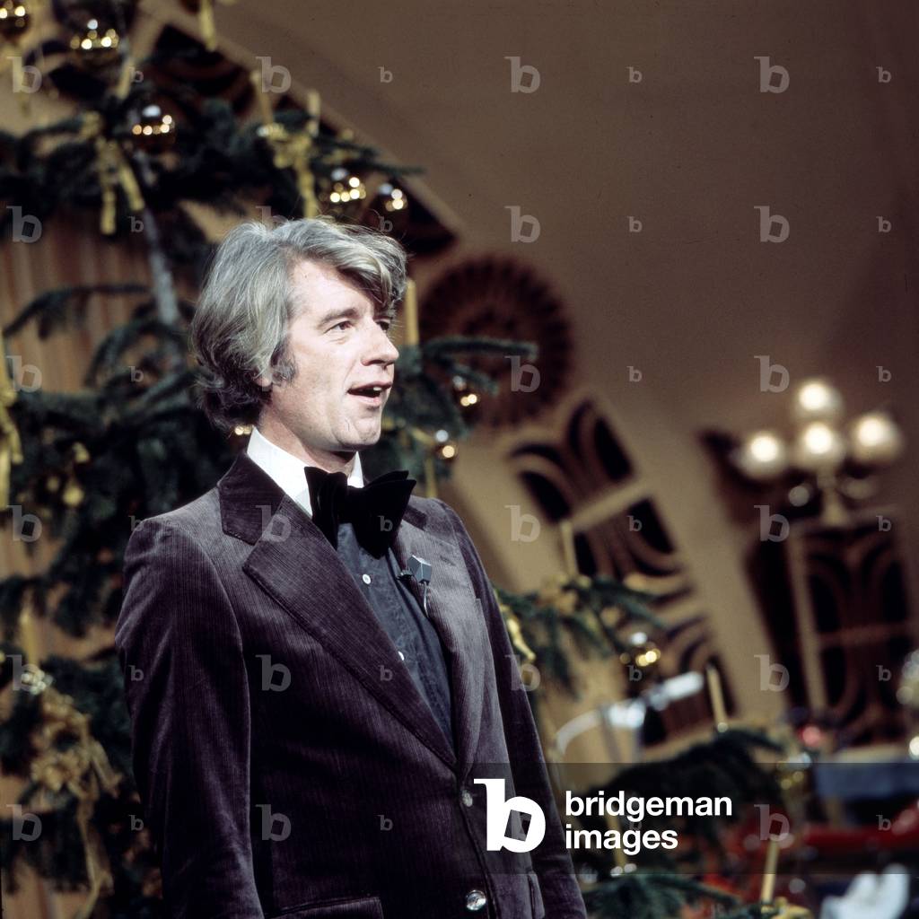 Dutch entertainer Rudi Carrell singing christmas carols under the christmas tree, Germany 1970s