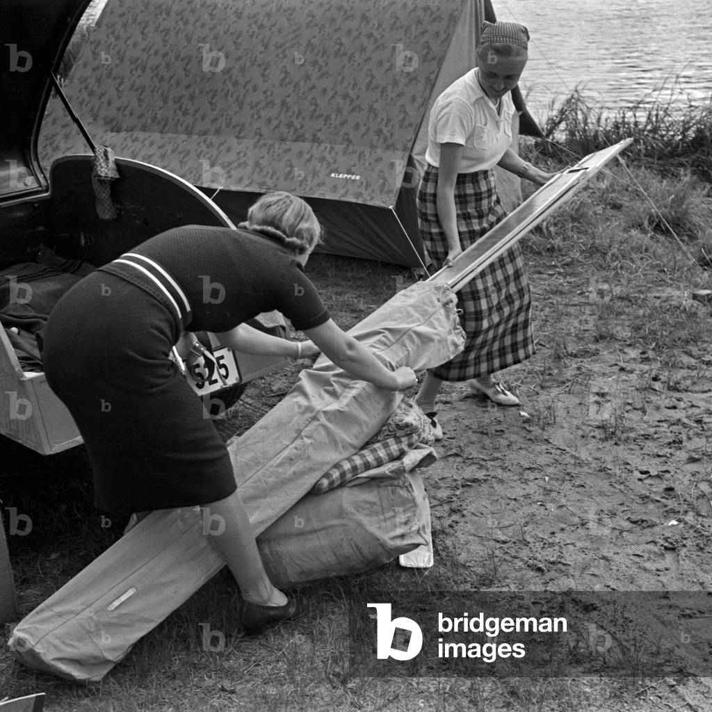 Two women packing the camping equipment after a vacation day at a lake, Germany 1930s (b/w photo)
