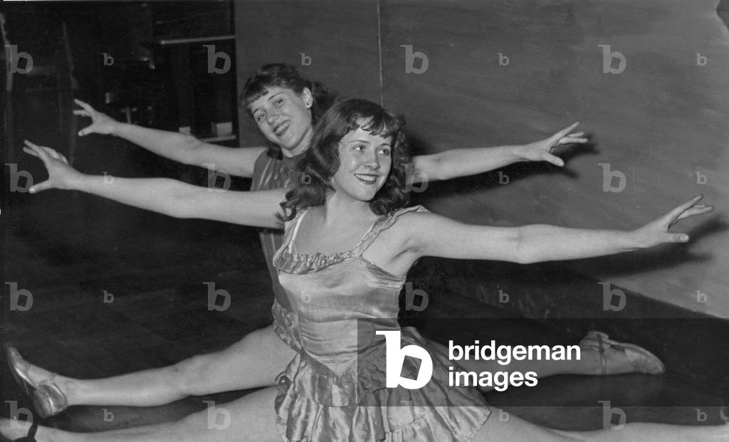 Two dancers of a ballet group do smiling the splits, 1950s