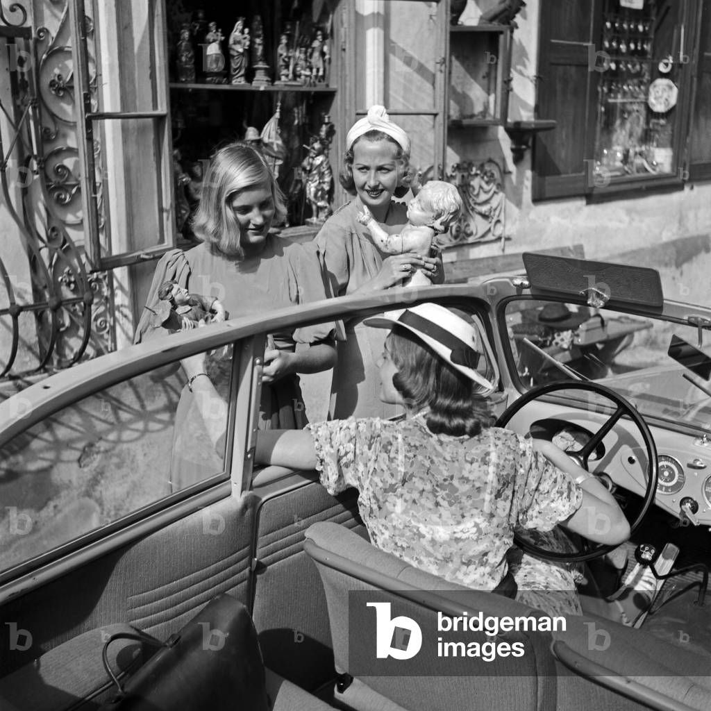 Three women chatting out from a convertible in front of a shop with craftwork, Germany 1930s (b/w photo)