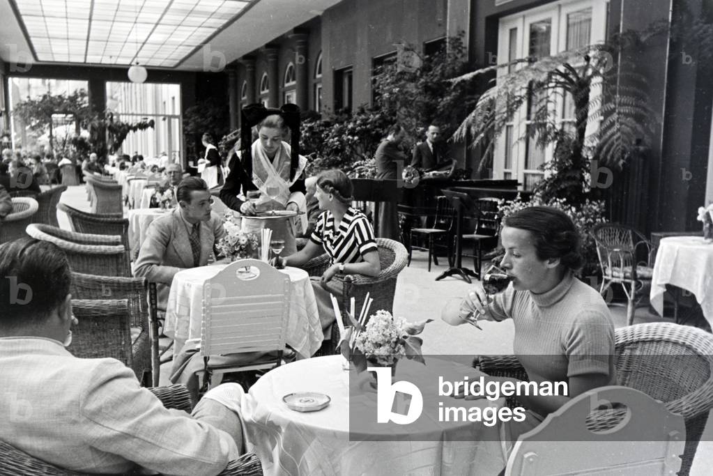 Visitors of the restaurant in the Kurhaus Casino in Baden-Baden are being served by waitresses wearing a traditional Black Forrest costume with the Bollenhut, Germany 1930s (b/w photo)