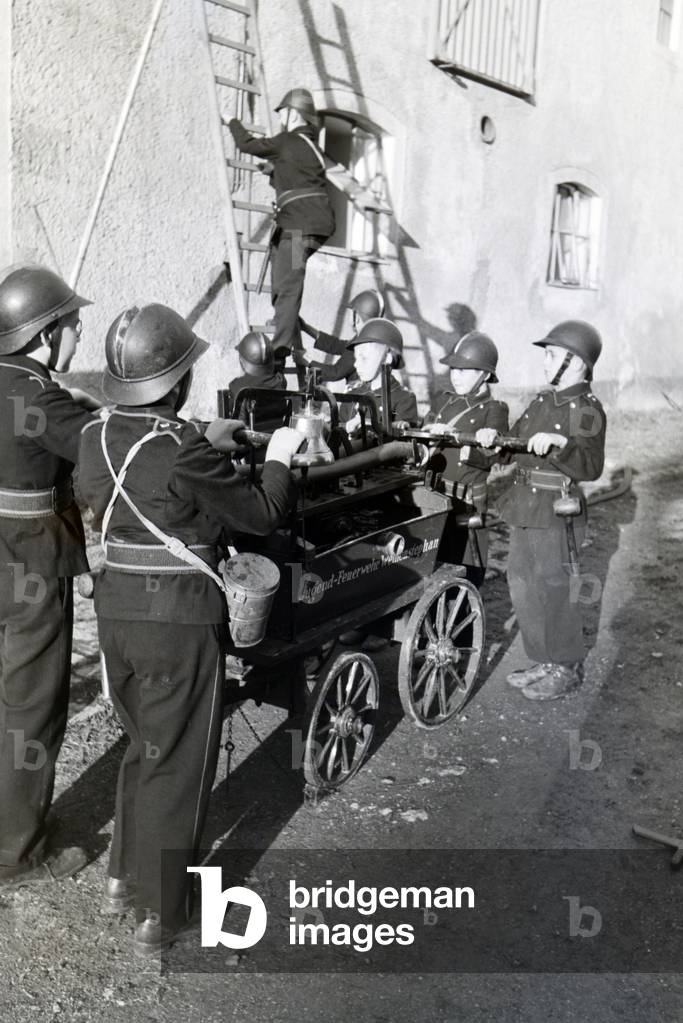 A group of junior firefighters is preparing the firewagon and ladder during a firefighter training, Germany 1930s (b/w photo)